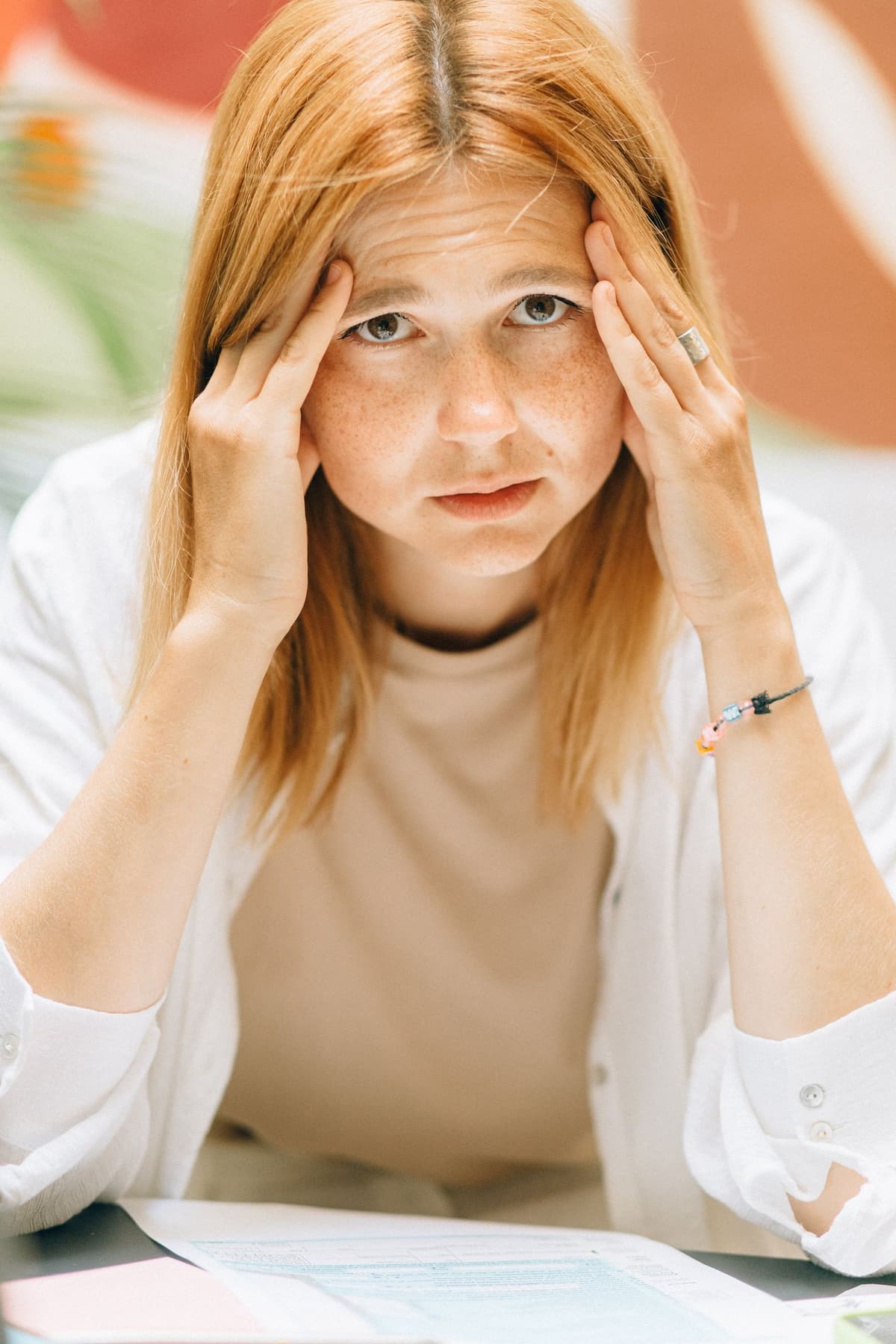 A person holding their temples while sitting at a desk.