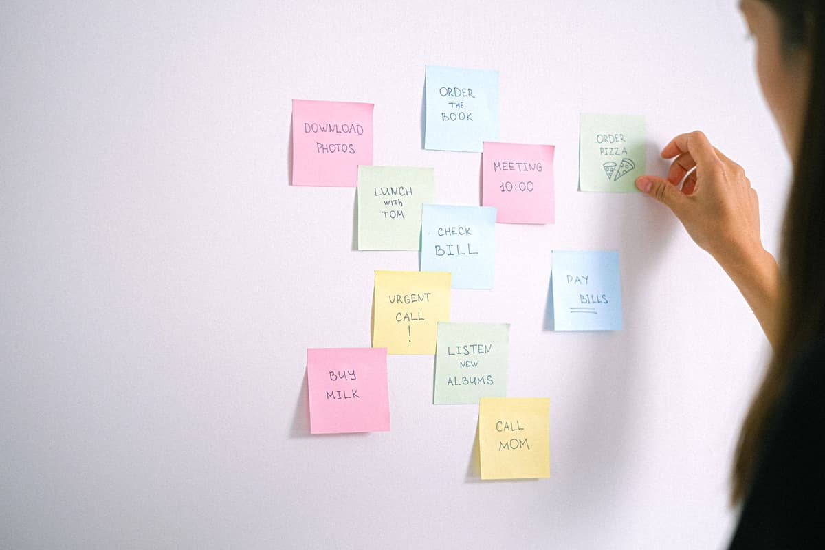 A person arranging colorful sticky-note reminders on a wall.
