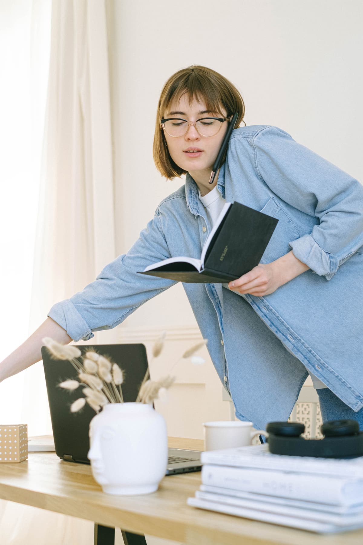 A person standing at a desk while talking on the phone and holding a notebook.