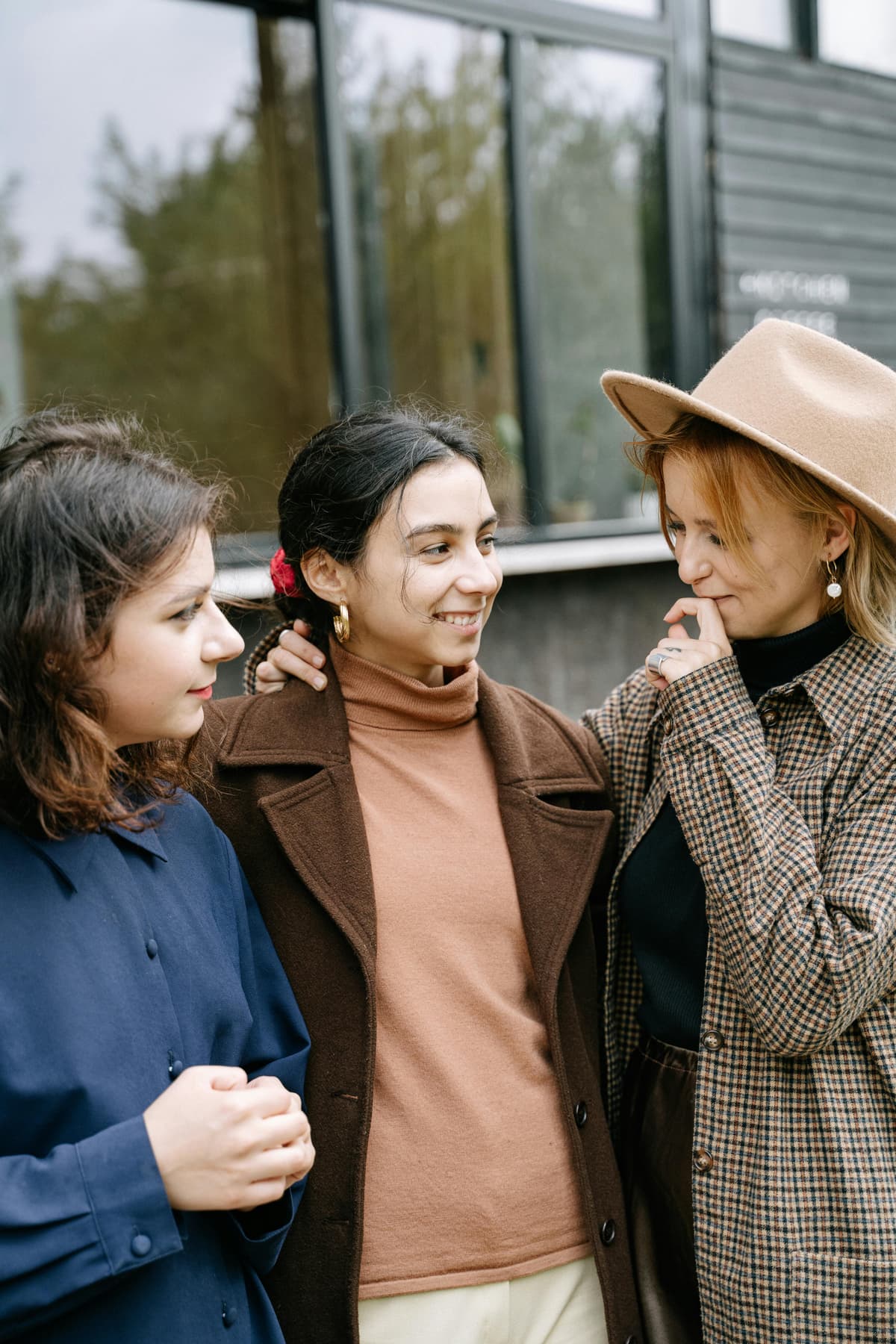 Three friends standing close together with their arms around each other outdoors.