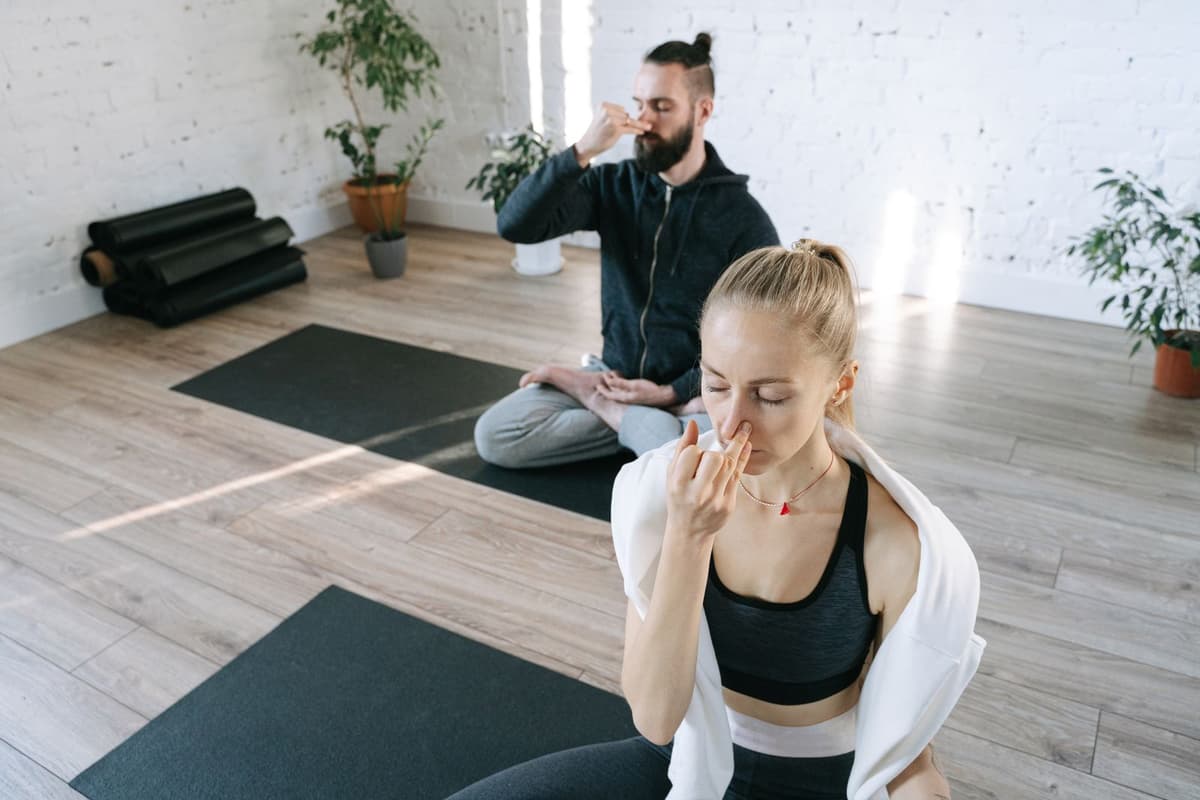 Two people practicing a slow breathing exercise in a bright studio.