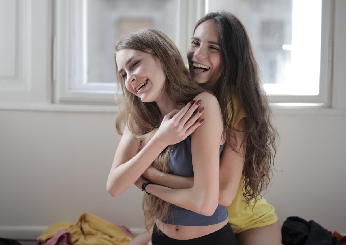 One person hugging another from behind in a bright room.