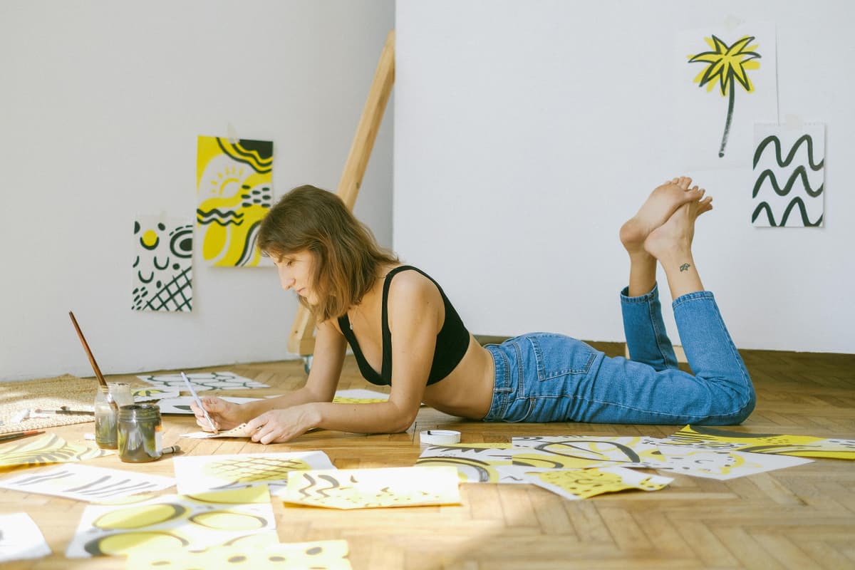 A person lying on the floor while drawing on large sheets of paper.