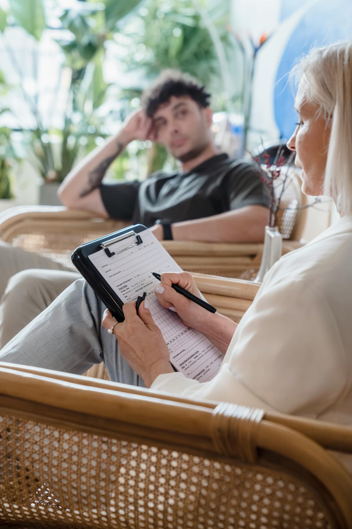 A therapist writing on a clipboard while speaking with a seated client.